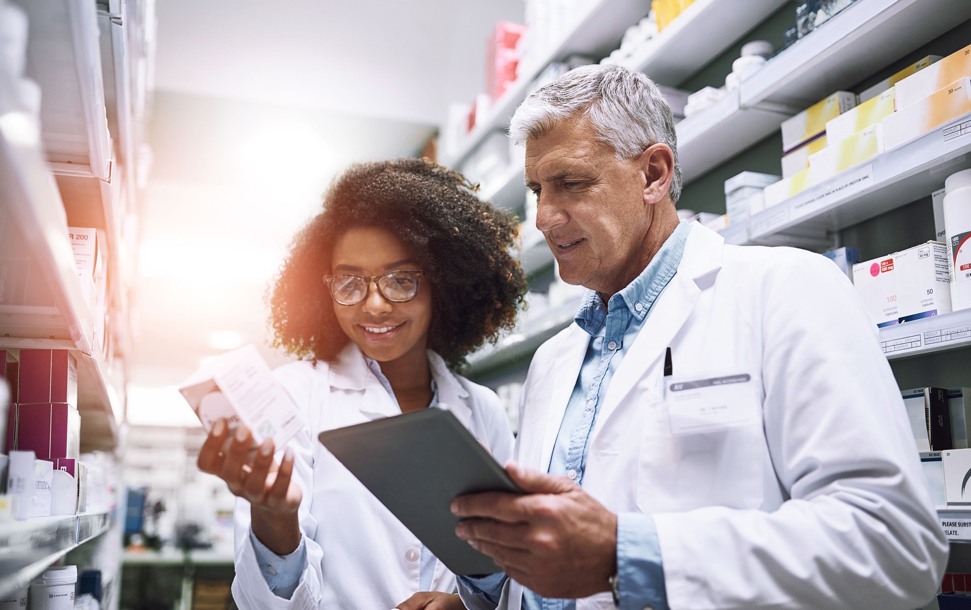Tablet, discussão e farmacêuticos com medicamentos em farmácia para inventário ou verificação de estoque. Saúde, estágio e mentor com estudante de farmácia para pesquisa médica em tecnologia digital